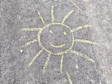 A cheerful yellow sun is sketched on rough asphalt, radiating positivity. The smiling face adds joy and warmth to a playful outdoor setting.の写真素材