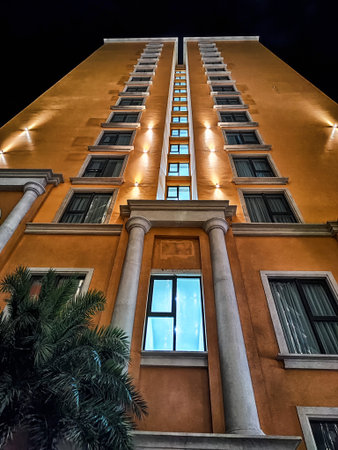 Nighttime view of a tall orange building, its windows glowing softly against the backdrop of a dark...
