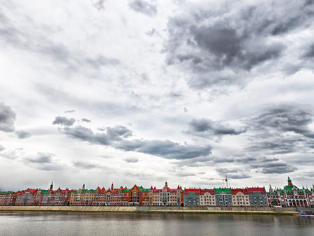 Embankment features colorful buildings reflecting in the river under a dramatic, cloudy sky.の写真素材