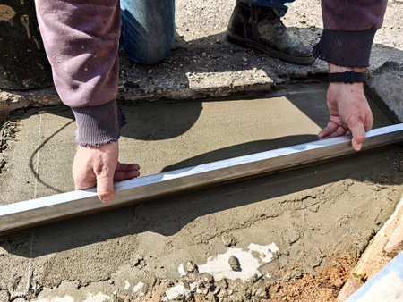 Men smoothing out wet concrete using a straight edge tool on a warm day at a construction location.の写真素材