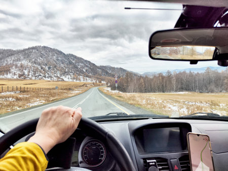 A driver navigates a winding road through mountainous terrain, showcasing early spring scenery and overcast skies.の写真素材