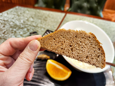 A person holds a slice of brown bread above a bowl of rice, accompanied by a vibrant orange wedge,...