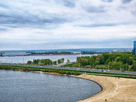 A tranquil riverbank with sandy beaches and lush greenery under a cloudy sky, showcasing a serene urban landscape in the evening.の写真素材