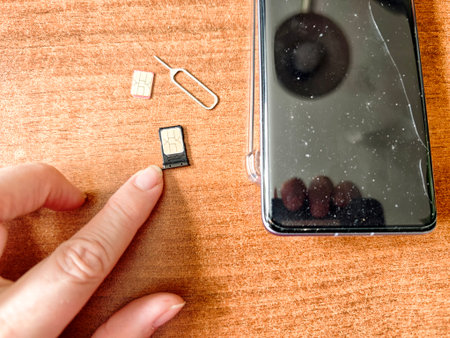 A hand points to two SIM cards and an eject tool next to a smartphone on a wooden surface during device setup.の写真素材