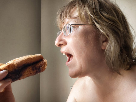 A middle-aged woman with disheveled hair is enjoying khachapuri after waking up in a relaxed morning atmosphere.の写真素材