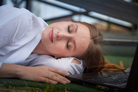 Young woman relaxing on grass with laptop during tranquil outdoor afternoon