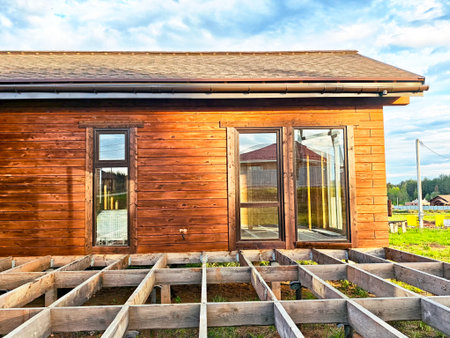New wooden cabin partially constructed, showcasing the foundation and large windows under a colorful sky during sunset.の写真素材