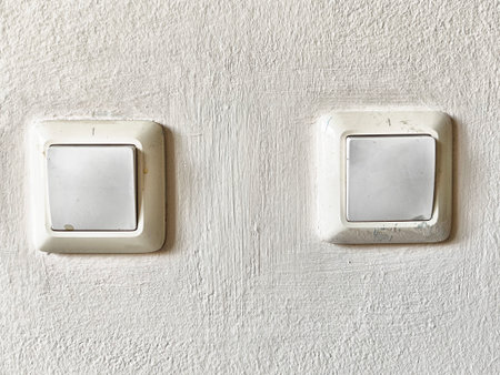 Bright daylight illuminates two light switches mounted on a textured wall, highlighting their clean and straightforward design.の写真素材