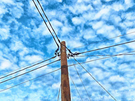 Tall wooden utility pole adorned with multiple power lines stretches upward against a backdrop of a...