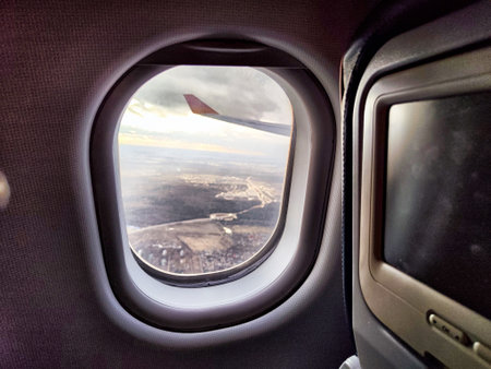 The airplane window frames a breathtaking view of distant mountains and rivers as the plane descends during late afternoon.の写真素材