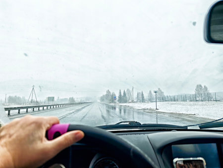 A person is steering a vehicle down a snowy road, facing challenges from low visibility and wet weather in a winter setting.の写真素材