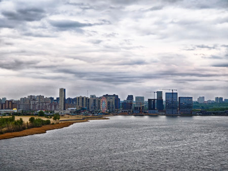 Urban skyline of Kazan viewed from the river, featuring modern buildings under a cloudy sky with...