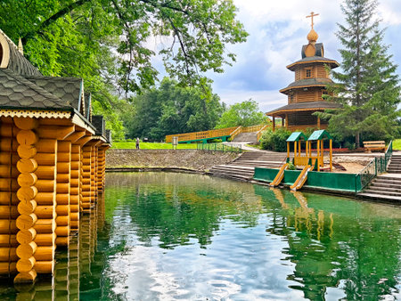 Lush trees frame charming wooden structures next to calm waters in a peaceful park, inviting relaxation and exploration on a sunny day.の写真素材