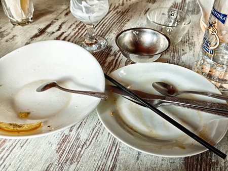 Dishes sit on a wooden table after a meal, featuring leftover food scraps and utensils used by...