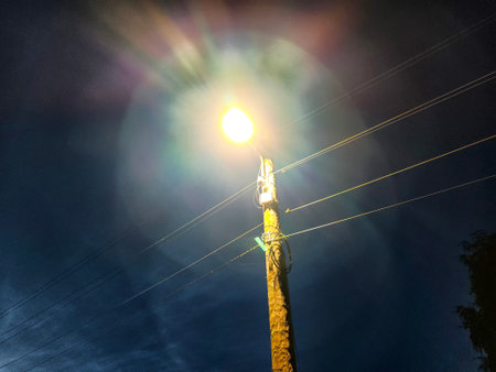 Utility workers are busy fixing a malfunctioning street light on a pole under a dark sky at night.