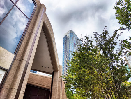 Tall buildings rise above lush greenery, with a stunning architectural entrance framed by clouds in...