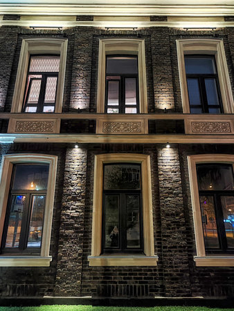 Illuminated bricks and windows highlight the architectural elegance of a historic building at night in a bustling city.の写真素材