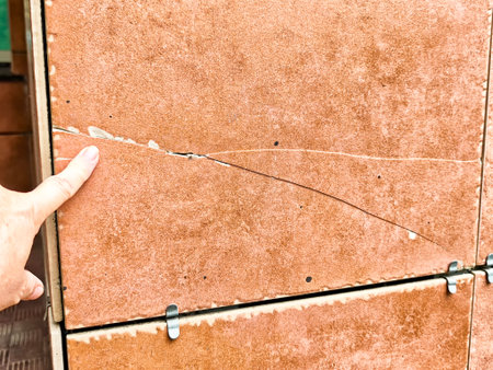 A person points at a cracked tile, highlighting visible damage in a construction area during the day.の写真素材