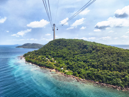 Enjoy breathtaking views from a cable car soaring above vibrant greenery and sparkling coastal waters on a clear day.の写真素材