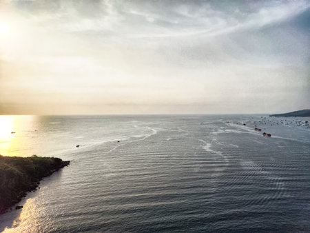 Beautiful sunset light reflects over tranquil waters as fishing boats dot the horizon near a rugged...