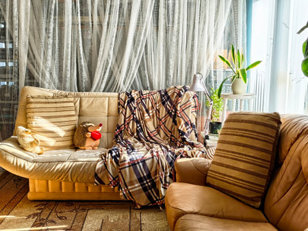 A cozy living room features a cream-colored couch draped with soft blankets, plush toys, and...