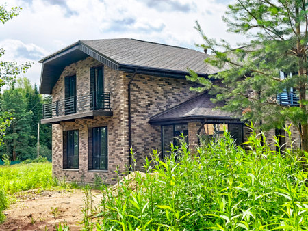 A modern brick house stands amidst lush green foliage, featuring large windows and a well-maintained yard in a tranquil area.の写真素材