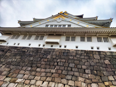 Osaka Castle showcases its beautiful layered roof design surrounded by ancient stone walls under a cloudy sky.の写真素材