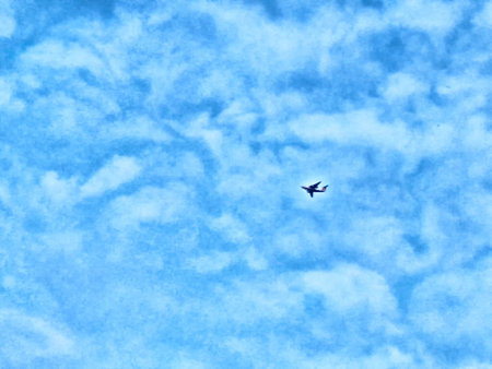 An airplane navigates through a bright blue sky filled with soft white clouds on a sunny day,...