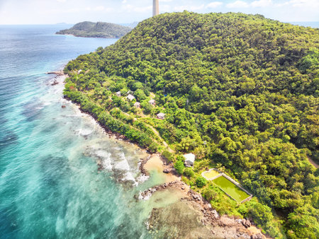Aerial view of a serene coastal area featuring green hills, rocky shores, and clear blue waters under bright sunlight.の写真素材