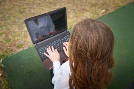 Young woman using laptop outdoors on a grassy surface during daytime for study or work