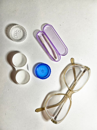 Eyewear accessories are arranged on a white surface, showcasing a pair of glasses, contact lens...