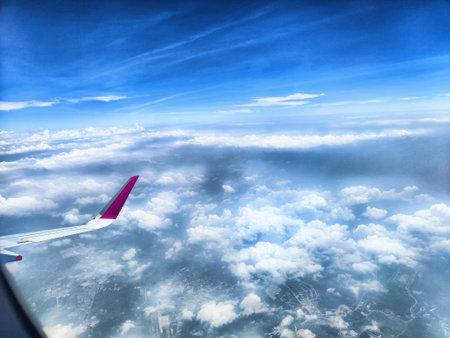 Flying high above the clouds, a vibrant airplane wing is visible against a backdrop of blue sky and billowing white clouds.の写真素材