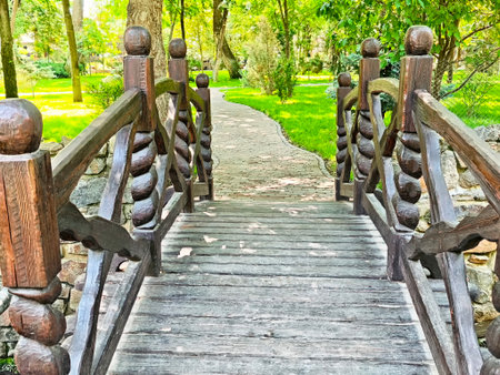 A charming wooden bridge connects pathways amidst vibrant trees and lush greenery, inviting...