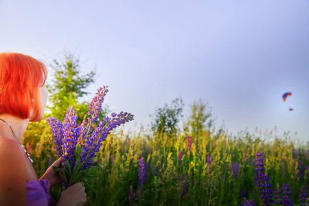 Woman holding purple flowers in vibrant meadow with balloon floating in the background during sunsetの写真素材