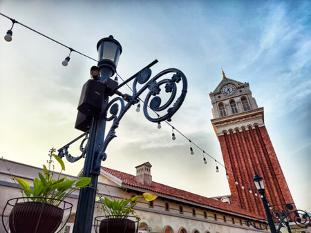 A striking clock tower dominates the skyline, surrounded by quaint buildings and decorative plants, with soft evening light enhancing the scene.の写真素材