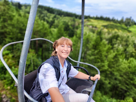 Smiling female traveler rides a cable car, surrounded by vibrant green mountains, capturing the moment in a selfie during her adventure.の写真素材