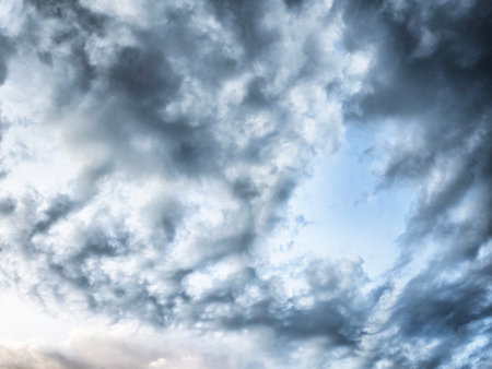 Thick, textured clouds swirl in varying shades of gray and blue as dusk approaches, creating a moody...