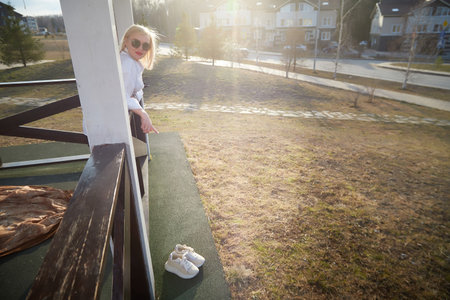 Woman enjoying sunlight on a balcony while pointing at shoes on the grass in a residential area during late afternoonの写真素材