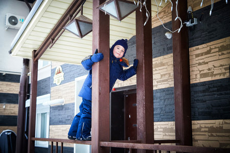 Child plays on wooden structure outside building during winter in snowy environment enjoying playground activitiesの写真素材