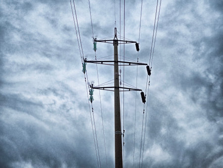 High voltage power lines stretch up to a cloudy sky with shades of grey, indicating possible rain during an overcast afternoon.の写真素材