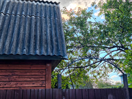 Wooden fence encloses a well-kept yard with a charming roof and lush greenery under a bright, sunny...