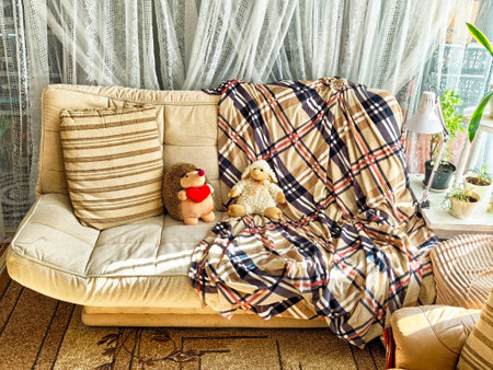 A sunny living room showcases a comfortable sofa adorned with a plaid blanket and two cute stuffed...