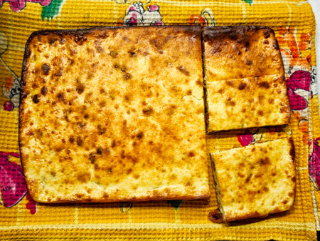 Freshly baked dish with a golden brown surface, placed on a vibrant towel with one portion removed for tasting.の写真素材