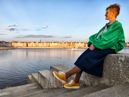 Person sitting on steps by a river with a vibrant city skyline at sunsetの写真素材