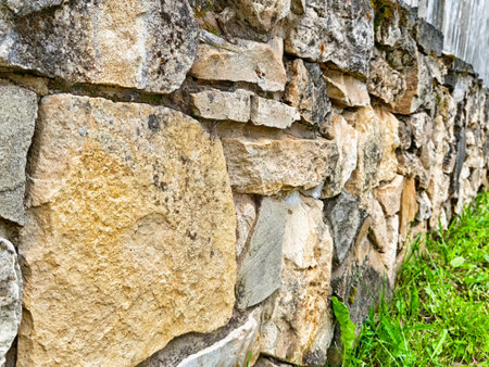 A sturdy stone wall showcases varied textures and colors, surrounded by vibrant green grass in a...