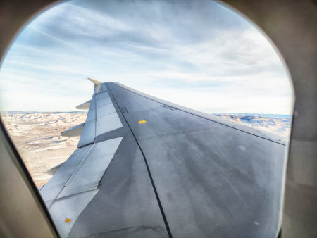 Airplane wing extends from window, showcasing a vast desert landscape below under a clear sky, highlighting the journey's elevation.の写真素材