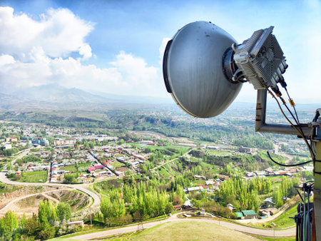 A communication tower stands tall, showcasing a vast green valley and a small town under a clear blue sky on a sunny day.の写真素材