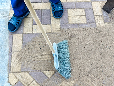 A person is diligently sweeping sand off a decorative pavement, ensuring cleanliness in the outdoor space during daylight hours.の写真素材