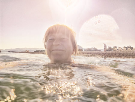 Woman with blonde hair smiles while swimming in clear water at the beach on a sunny day during a travel adventure.の写真素材