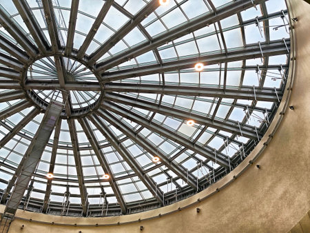 A circular glass ceiling showcases intricate design and modern lights in a spacious indoor setting,...